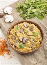 Lentils porridge with champignons and coriander in a wooden bowl on a white wooden background and