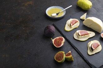 Summer appetizer with pear, cottage cheese, figs and honey on slate board on a black concrete