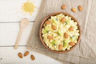 Millet porridge with kiwi and almonds in wooden bowl on a white wooden background and linen textile