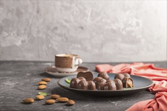 Chocolate caramel candies with almonds and a cup of coffee on a black concrete background and red