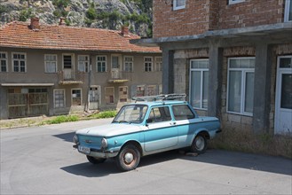 A blue retro car parked in front of dilapidated buildings under a clear sky, Zaporozhets 968,