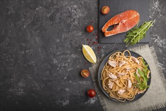 Semolina pasta with salmon and salmon steak on a black concrete background and linen textile. Top