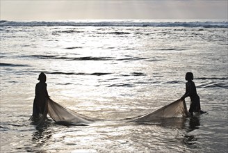 Silhouette of two girls fishing bichiques on the Indian ocean coast, Mananjary, Madagascar.