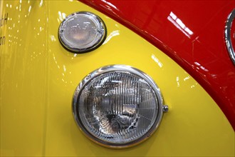 The front end of a Volkswagen bus with indicators and headlights. Techno Classica is the trade fair