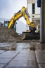 A yellow excavator doing earthworks on a construction site next to a building, Hermann Hesse