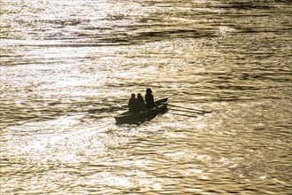 Rowing boat, 3-seater, on a river, reflecting sun on the water surface