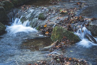 Small waterfall of the Leutra stream flowing over moss-covered stones, framed by foliage and