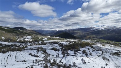 Snow-covered landscape with scattered green fields and a distant village under a cloudy sky. Posof,