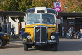 Front view of a yellow vintage bus with people in an urban environment, vintage car, Saurer,