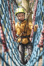 Portrait of cute little boy walk on the net in an adventure rope park