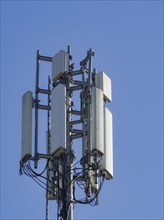 A close-up of a cell tower with antennas against a bright blue sky