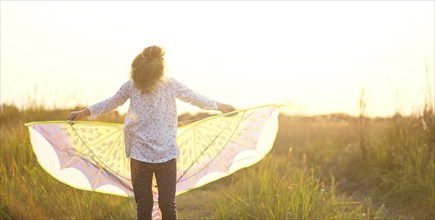 Girl is standing with wings in field, learning to fly a kite, Outdoor entertainment in summer,