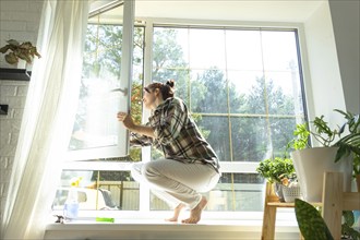 Woman manually washes the window of the house with a rag with spray cleaner and mop inside the