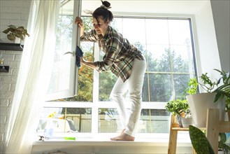 Woman manually washes the window of the house with a rag with spray cleaner and mop inside the