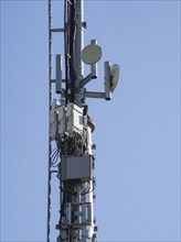 Telecommunication tower against a clear blue sky, featuring antennas, microwave dishes, and