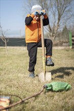 Six-year-old boy in the garden plants tree during sunny spring day.