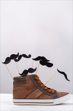 Vertical shot of brown sneaker with cartoon moustaches. Mens shoe with copy space on white