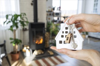 Key to house with keychain against background of fireplace stove with fire and firewood. Cozy home