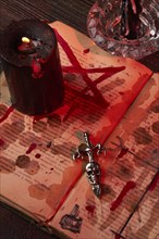 Vertical shot of antichrist cross on the satanic bible stained with blood. Burning black candle on