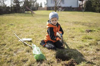 Six-year-old boy in the garden plants tree during sunny spring day.