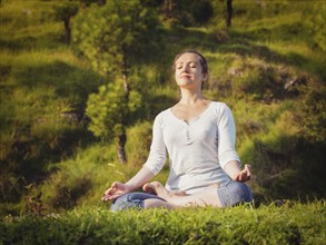 Young sporty fit woman doing yoga outdoors, meditating and relaxing in Padmasana Lotus Pose) with