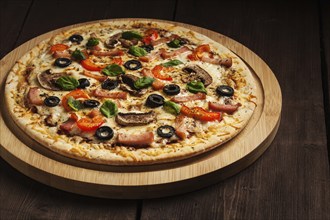 Ham pizza with (capsicum), mushrooms, olives and basil leaves on wooden board on old table