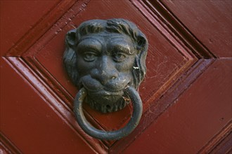 Traditional metal lion's head door knocker on a red wooden door, detail, Klingenstein Castle,