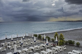 White reclining chairs on deserted beach during bad weather with dark, menacing rain clouds over