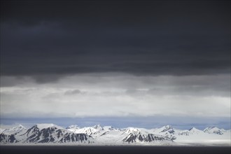 Black rain clouds over snow covered mountains along Isfjorden, second longest fjord at Spitsbergen,