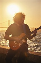 Hipster street musician in black playing electric guitar in the street on sunset