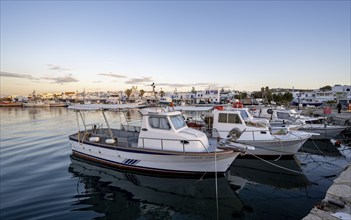 Fishing boats in the harbour of Naoussa at sunset, reflected in the sea, White Cycladic houses,