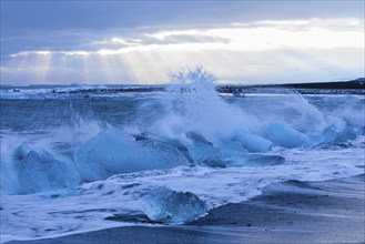 Waves breaking on icebergs on the black beach of Breidamerkursandur, near Jökullsarlon, Sudurland,