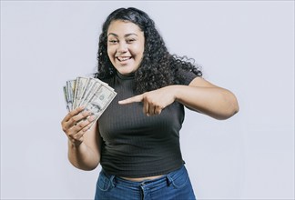 Attractive latin girl holding and pointing money. Smiling young woman holding and pointing money