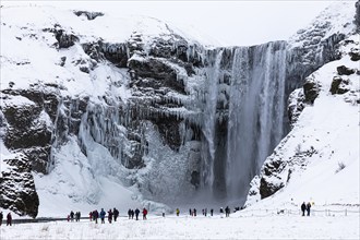 Tourists at Skogafoss waterfall, snowy and icy rock face, Sudurland, Iceland, Europe