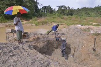 Diamond hunters digging a pit with shovels, supervisor holding a parasol, left, near Koidu,