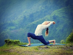 Yoga outdoors, sporty fit woman practices Hatha yoga asana Anjaneyasana, low crescent lunge pose