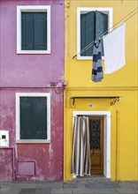 Purple and yellow house facade with entrance door and windows and clothesline, colourful houses on