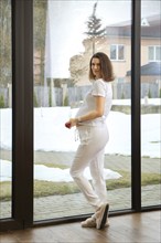 Beautiful pregnant woman standing by the window at home