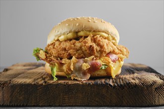 Chicken burger with bacon and cheese on wooden board, front view