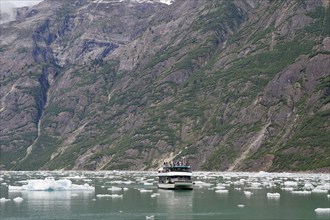 Small boat in front of high mountains and ice floes of a glacier calving into the sea, Tracy Arm