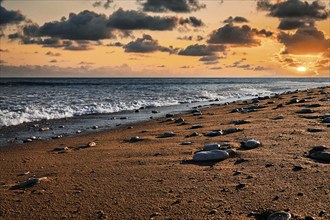 Pebbles glistening on empty sandy beach, cloudy sky at sunset, backlight, Oleron Island, Île