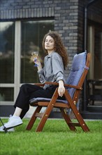 Beautiful young woman sits on chair on backyard