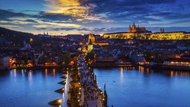 Panorama of illuminated Prague castle and Charles Bridge with tourist crowd over Vltava river in