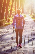 Nordic walking adventure and exercising concept, woman hiking with nordic walking poles in park.