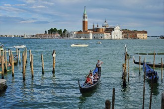 VENICE, ITALY, JUNE 27, 2018: Gondolier with tourists in gondola in lagoon of Venice by Saint Mark