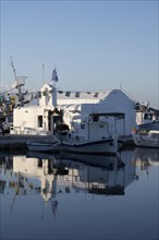 White Cycladic Greek orthodox church Agios Nikolaos, decorated with flags, harbour of Naoussa,