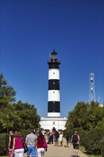 Pedestrians in the garden at the black and white Chassiron lighthouse, Saint-Denis-dOléron, Oleron