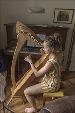 Young woman playing the harp at home, Mecklenburg-Vorpommern, Germany, Europe