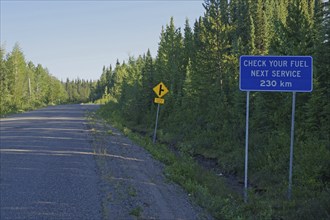 Narrow, traffic-free road and a sign pointing to the next petrol station, mountain landscape,