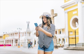 Female tourist texting phone in the square of Granada. Smiling young tourist in hat using cell